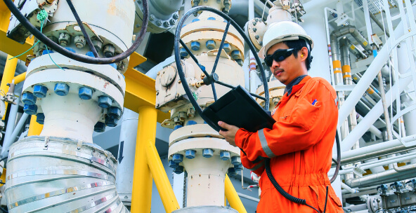 Man in industrial facility wearing an orange jumpsuit and hard hat with tablet in his hands