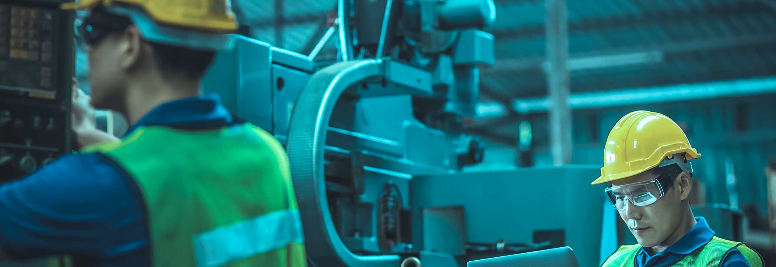 Engineer in hardhat with a tablet computer reviewing data while their coworker is reviewing the machine in an industrial facility.