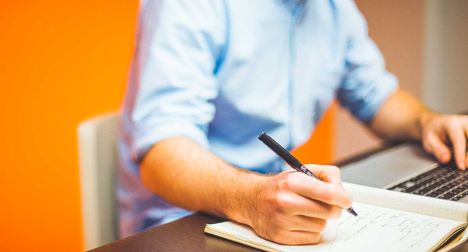 Man taking notes while working on computer in conference room