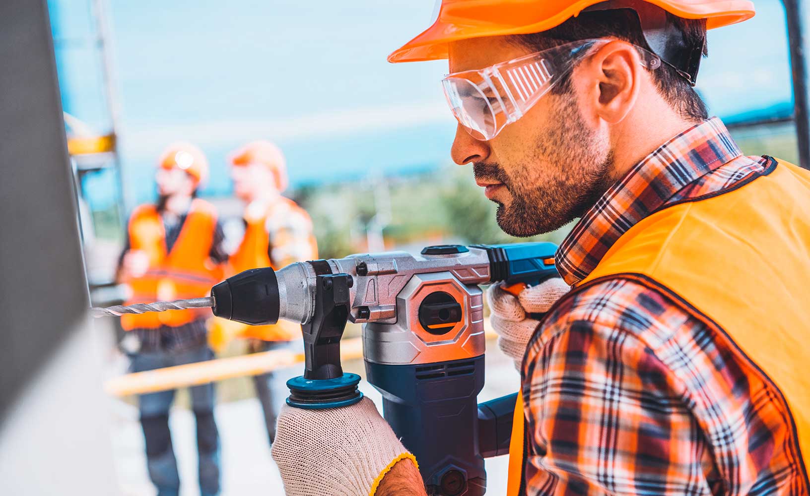 Bauarbeiten mit tragbaren Geräten an der Seite eines Gebäudes mit Mitarbeitern im Hintergrund auf der Baustelle.